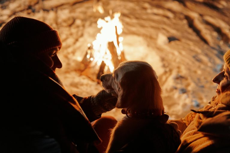 Friluftsliv A couple enjoys a warm winter night by a bonfire, accompanied by their dog amidst a snowy setting.